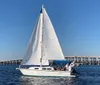 A sailboat with its sails fully unfurled glides through the water near a long bridge under a clear blue sky