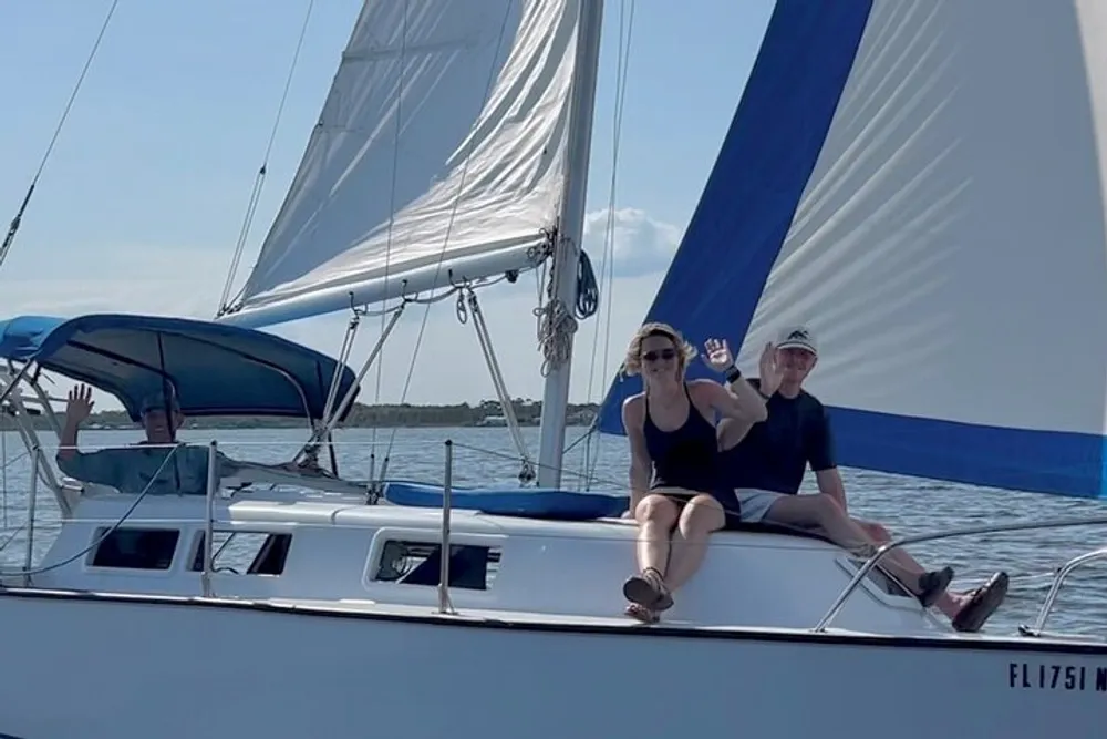 Three people are enjoying a sunny day while sailing on a blue and white sailboat