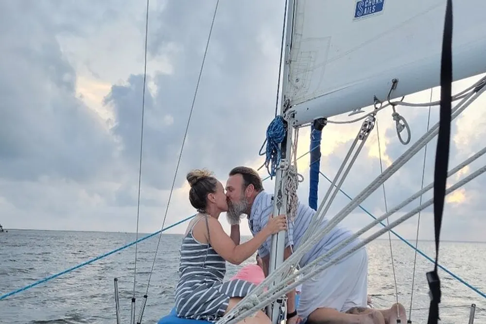 Two people are sharing a kiss on a sailboat against a backdrop of an overcast sky