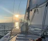 A sailboat with its sails fully unfurled glides through the water near a long bridge under a clear blue sky