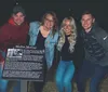 Four individuals are smiling for a photo at night with one of them holding a sign about a historical figure named Mollie McCoy