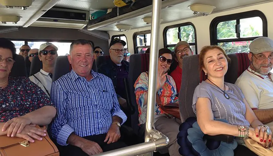 A group of cheerful people are seated inside a bus, smiling and looking towards the camera, appearing to be on a shared journey or tour.