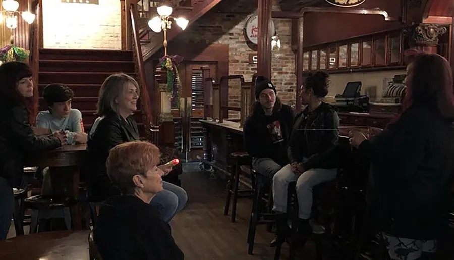 A group of people are casually gathered inside a cozy-looking bar with brick walls and vintage decor, engaged in conversation and relaxation.