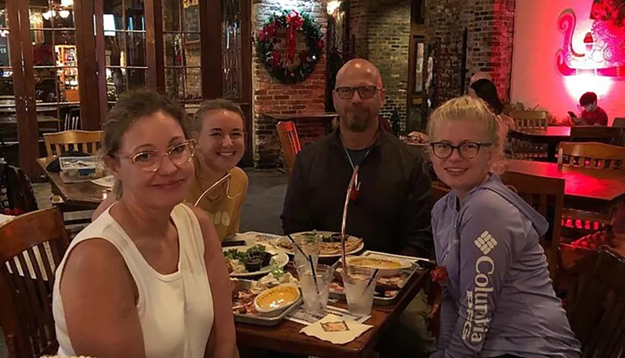 A family of four is smiling at the camera while sitting at a restaurant table with plates of food in front of them.