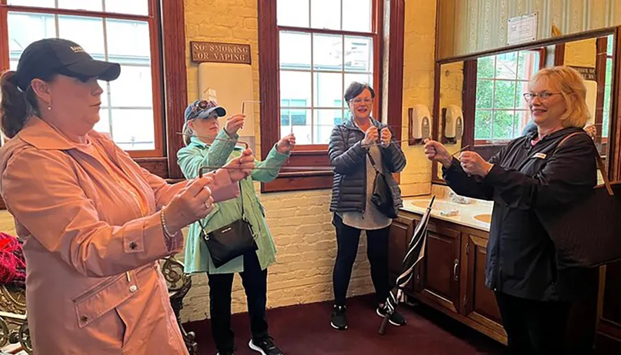 Four women are smiling and holding strings attached to what appear to be chocolate bars in a room with a vintage aesthetic.