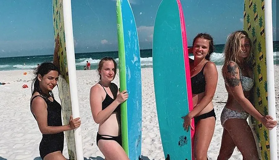 Four people are posing with colorful surfboards on a sunny beach.