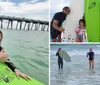 A smiling person is giving a thumbs-up while lying on a green surfboard in the water near a pier