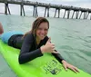 A smiling person is giving a thumbs-up while lying on a green surfboard in the water near a pier