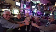 A group of five cheerful people are toasting with shot glasses at a bar with a festive atmosphere.