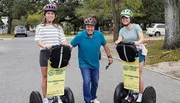 Three people are smiling and standing with Segways on a street, likely prepared for a guided tour.
