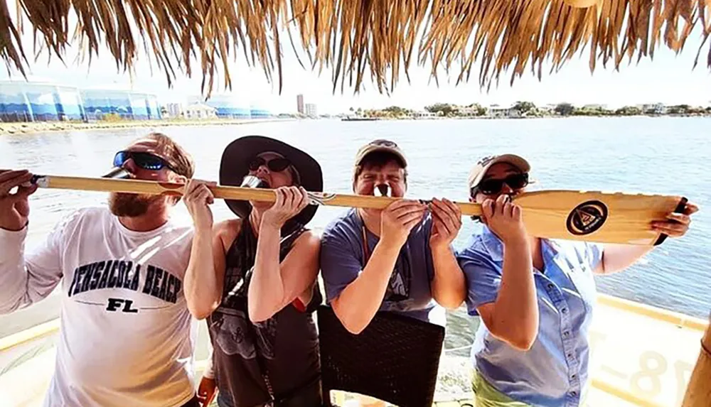 A group of people is playfully biting down on a single oar under a thatched roof possibly indicating a comical or lighthearted moment during a boating or beach activity