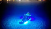Two people are kayaking at night with underwater lights illuminating the water around them, creating a glowing effect.