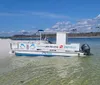 A pontoon boat is moored along a sandy beach under a clear sky with a person seen sitting at the rear of the boat