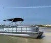 A person is standing on a pontoon boat with a red bimini top anchored in calm waters under a clear blue sky