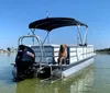 A person is standing on a pontoon boat with a red bimini top anchored in calm waters under a clear blue sky