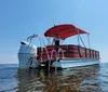 A person is standing on a pontoon boat with a red bimini top anchored in calm waters under a clear blue sky