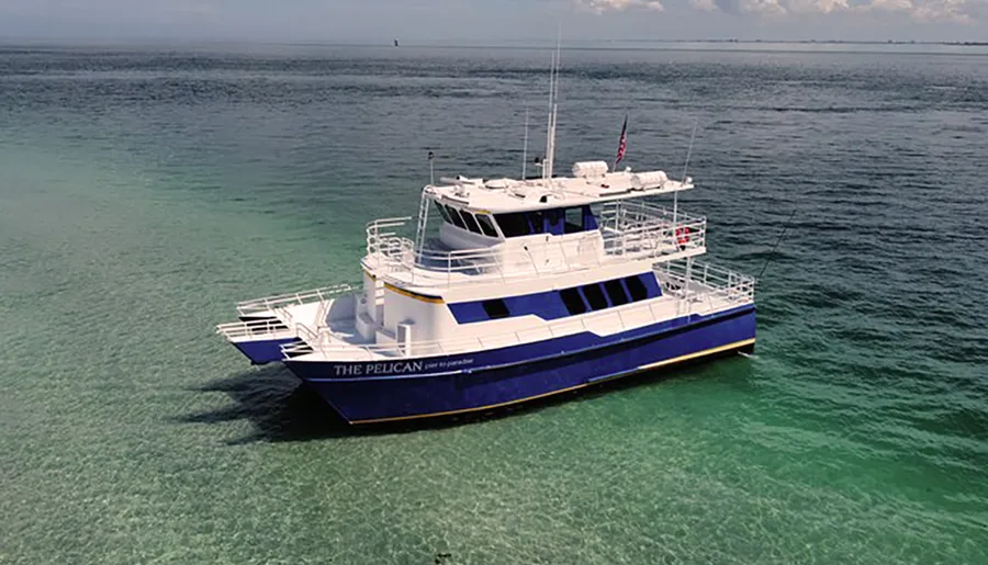 A blue and white boat named THE PELICAN is anchored in clear, shallow waters.