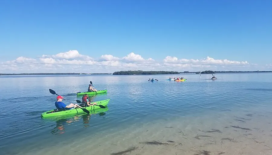 People are kayaking on a calm blue lake under a partially cloudy sky.