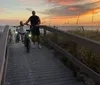 Two people on bicycles are enjoying a scenic sunset by the beach on a wooden boardwalk