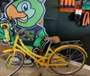 A cutout of an anthropomorphic frog character holding a spray paint can is positioned as if it is riding a real yellow bicycle within a store