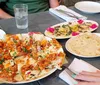 A person with painted fingernails is seated at a table with various dishes including what appears to be a pizza and flatbread ready to dine