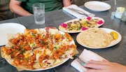 A person with painted fingernails is seated at a table with various dishes, including what appears to be a pizza and flatbread, ready to dine.