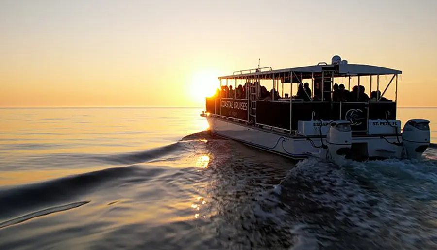 A group of people enjoy a sunset cruise on a calm sea aboard a double-decker pontoon boat.