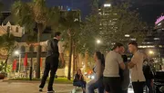 A person is performing a slackline walk in an urban night setting while onlookers watch.