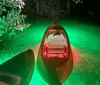 A kayak is illuminated from within casting a vibrant glow on the surrounding waters at night