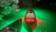 A kayak is illuminated from within, casting a vibrant glow on the surrounding waters at night.