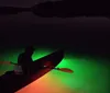 A kayak is illuminated from within casting a vibrant glow on the surrounding waters at night