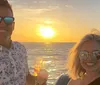 A smiling man and woman are enjoying a sunset on a boat holding glasses of wine
