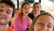 Four cheerful friends are taking a close-up selfie, with one making a peace sign, another sticking out her tongue, and all of them seemingly enjoying a fun moment together.