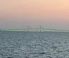 The image shows a tranquil expanse of water with a long bridge illuminated in green lights stretching across the horizon under a dusky sky