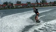 A person is wakeboarding on a body of water with houses in the background.