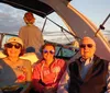 Three people are smiling for the camera while enjoying a boat ride at sunset with another person facing away toward the water