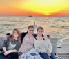 Three individuals are smiling on a boat with a beautiful sunset over the ocean in the background