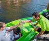 Two individuals are riding a green mini powerboat in a marina with other boats and yachts docked in the background