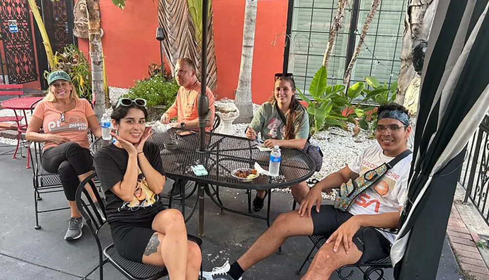 A group of five people is enjoying time together at an outdoor dining area with bright smiles and casual attire