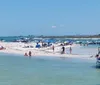 A group of people is enjoying a sunny day in shallow waters beside a boat with some holding beverages and the coastline visible in the background