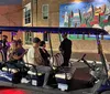 A group of six smiling people pose in front of a colorful mural that says City of TAMPA with a golf cart-style vehicle parked to their right in what appears to be an urban setting at night