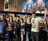 A group of six smiling people pose in front of a colorful mural that says City of TAMPA with a golf cart-style vehicle parked to their right in what appears to be an urban setting at night