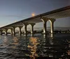 A large bridge with illuminated arches spans over shimmering water at twilight