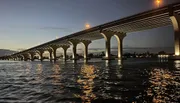 A large bridge with illuminated arches spans over shimmering water at twilight.