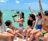 A group of people are enjoying a sunny day on a boat with one raising her arm in excitement and another drinking from a bottle amidst a backdrop of clear turquoise waters and other boats