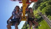 A group of people are enjoying a thrilling ride on a roller coaster, with bright expressions as they soar above the tracks against a clear blue sky.