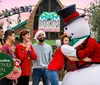 A group of people wearing festive Christmas attire is happily interacting with a person in a snowman costume at Busch Gardens Christmas Town event