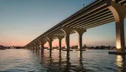 A long bridge spans across tranquil water with a backdrop of a twilight sky.