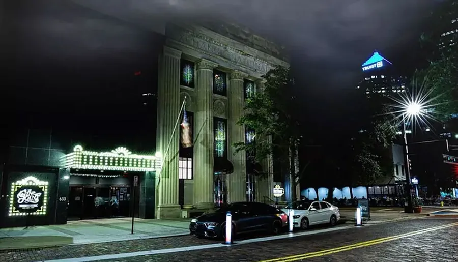 The image depicts a well-lit, classic-style building at night, showcasing an illuminated marquee and surrounded by modern cars and urban street elements.