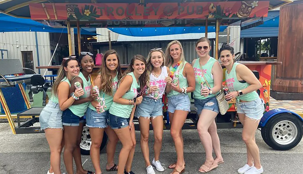 A group of smiling friends pose together in matching tops in front of a Trolley Pub venue during what appears to be a festive social outing